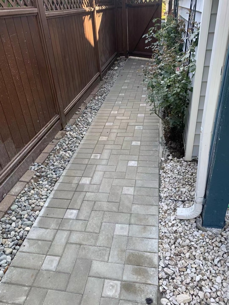 Paver path between wood fence and house with river rock borders