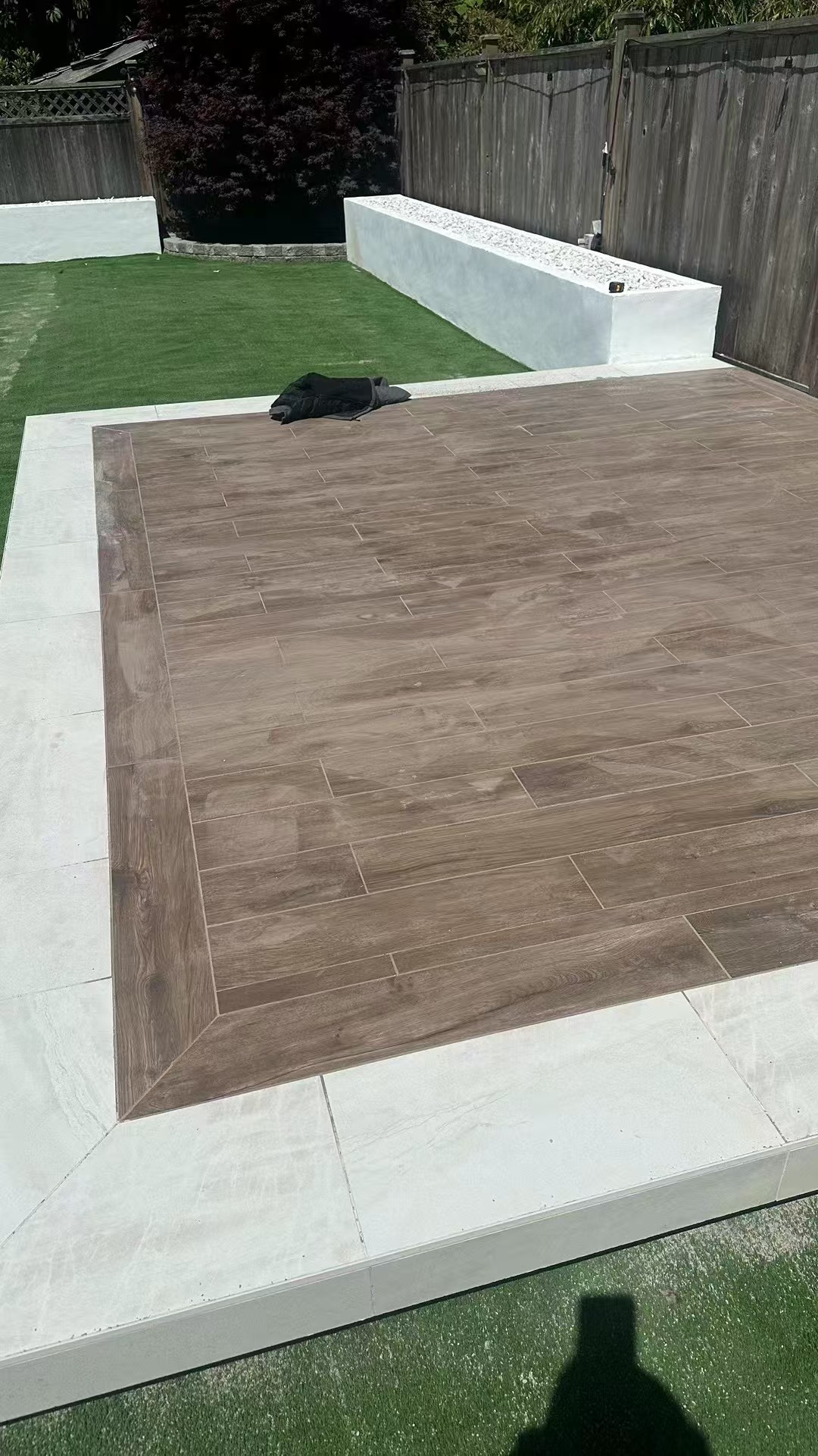 Modern wood-look tile patio with white stone border and raised planter